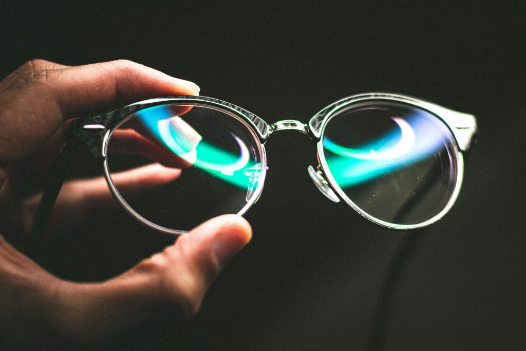 Closeup of crop anonymous person showing eyeglasses with stylish spectacle frame on black background